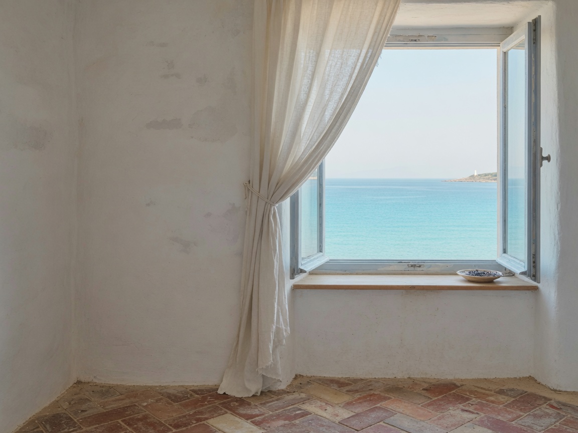 A whitewashed room with an open window looking onto a calm sea